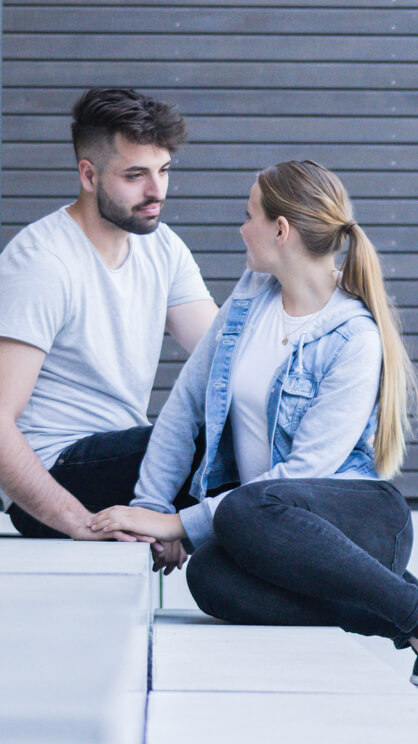 Ein junger Mann und eine junge Frau sitzen auf einer Treppe und schauen sich an